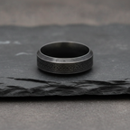 dark grey stainless steel ring with intricate Viking designs on a dark stone surface