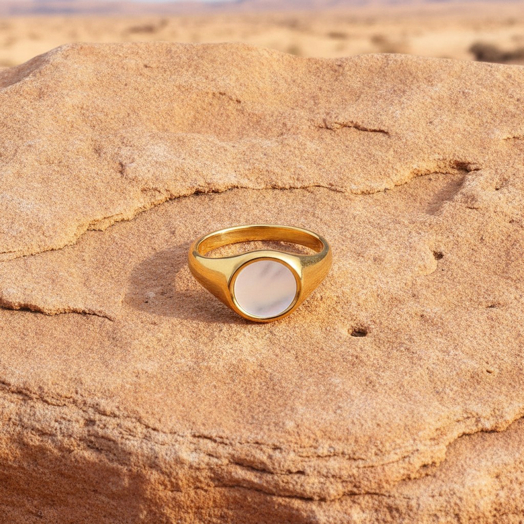 Gold ring with a circular stone on a textured ssandstone surface