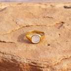 Gold ring with a circular stone on a textured ssandstone surface