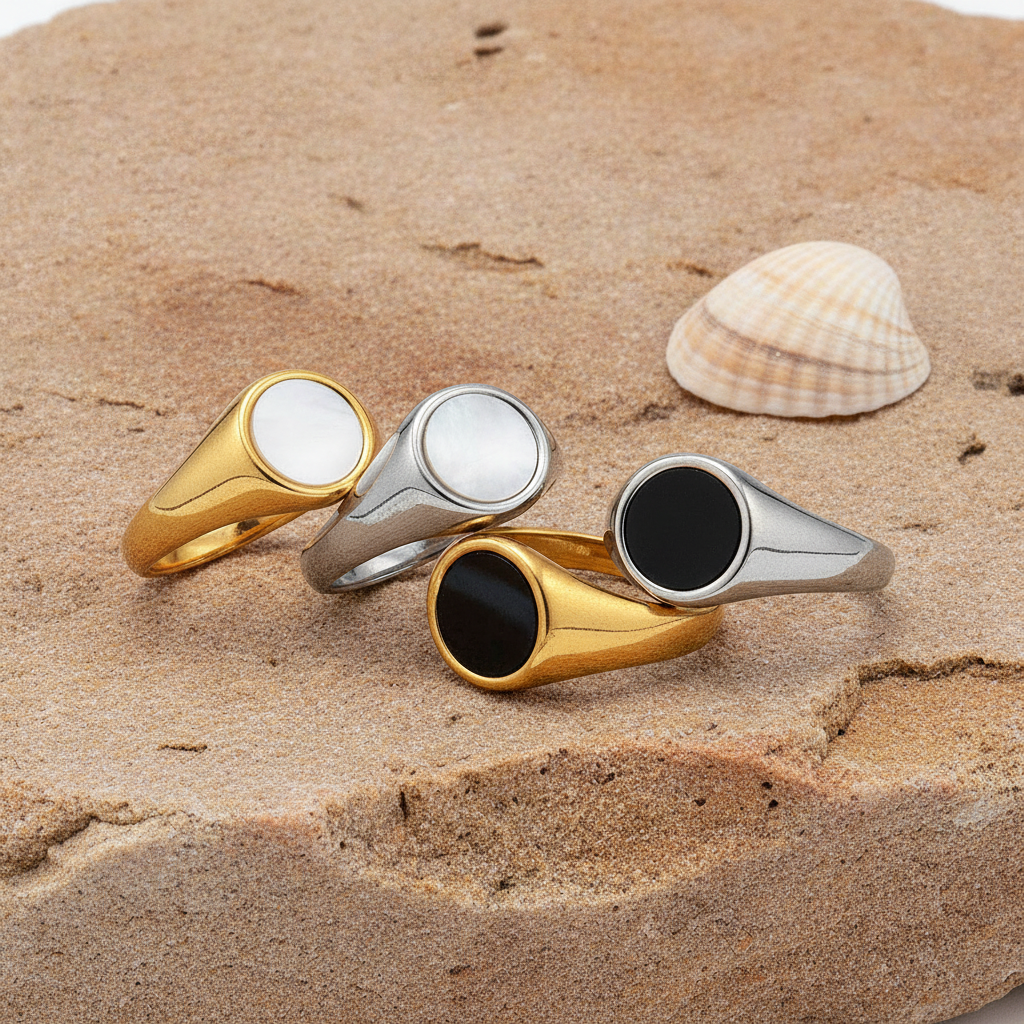 Four rings in gold and silver on a sandy surface with a shell.