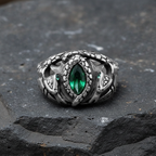 Silver ring with a green gemstone and twin serpent design on a dark basalt stone surface