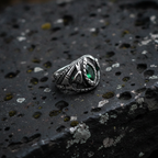 Silver snake ring with green gemstone on a textured black surface