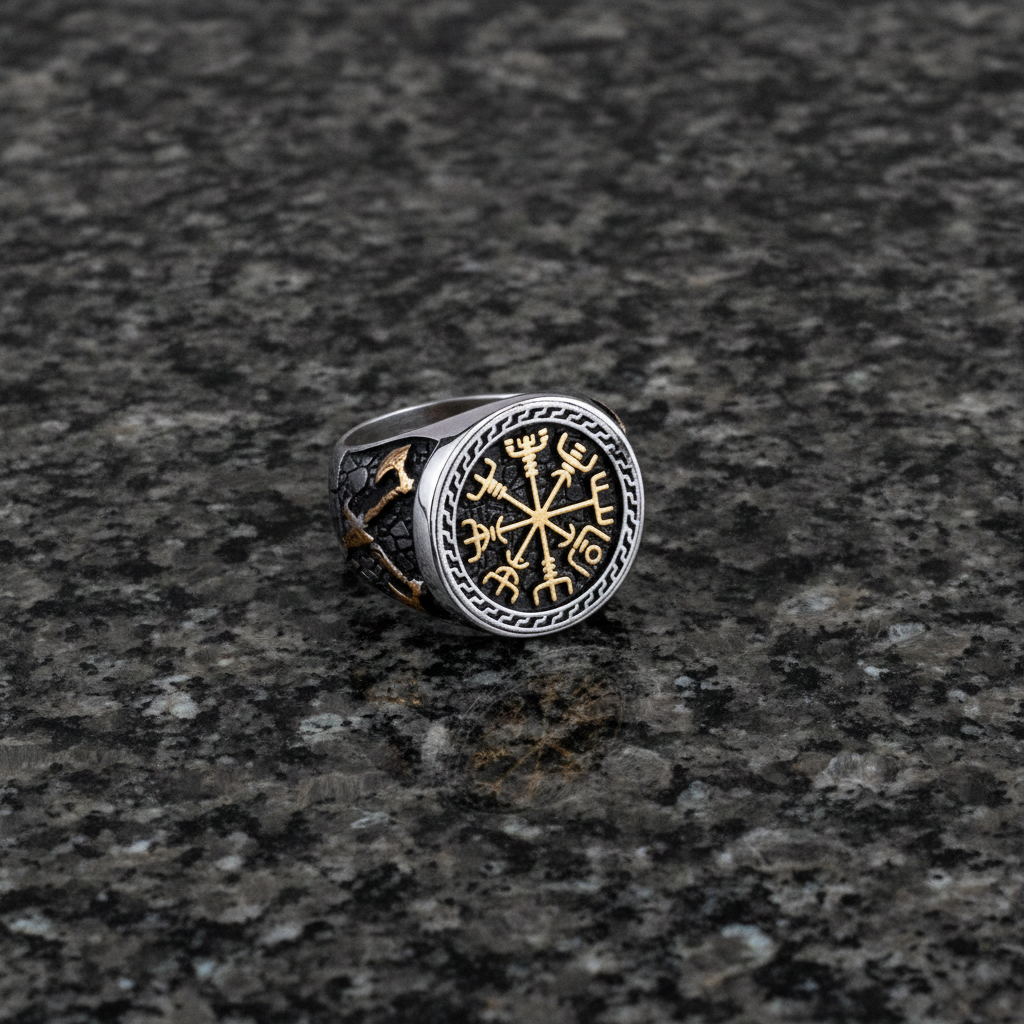 A silver and gold Viking signet ring with a intricate Vegvisir design on a dark grey granite stone surface