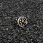 A silver and gold Viking signet ring with a intricate Vegvisir design on a dark grey granite stone surface