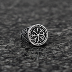 A silver Viking signet ring with a intricate Vegvisir design on a dark grey granite stone surface
