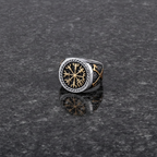 A silver and gold Viking signet ring with a intricate Vegvisir design on a dark grey granite stone surface