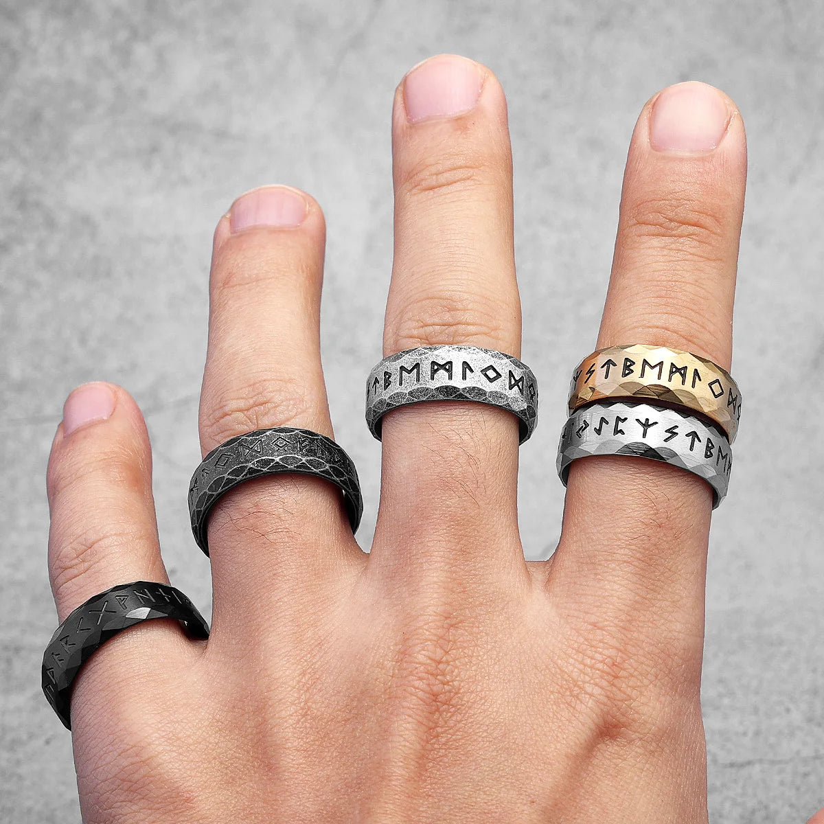 Hand wearing multiple Viking styled rings with different designs on a gray background