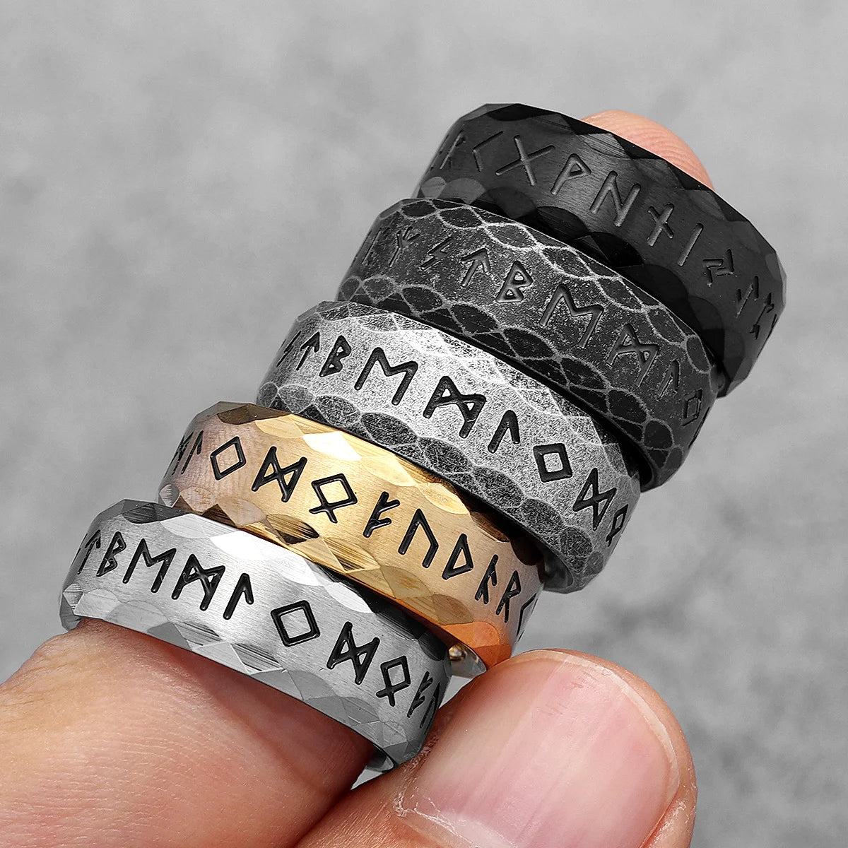 Stack of Nordic rings with engraved text on a finger against a grey background