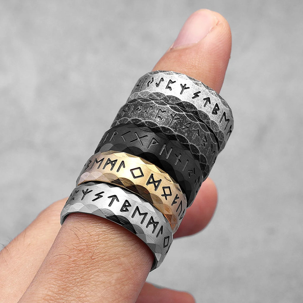 Three metallic rings with engraved patterns on a finger against a grey background