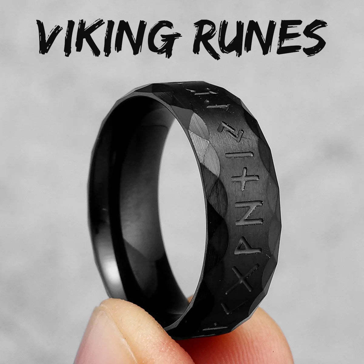 Black ring with engraved text held by a hand against a grey background