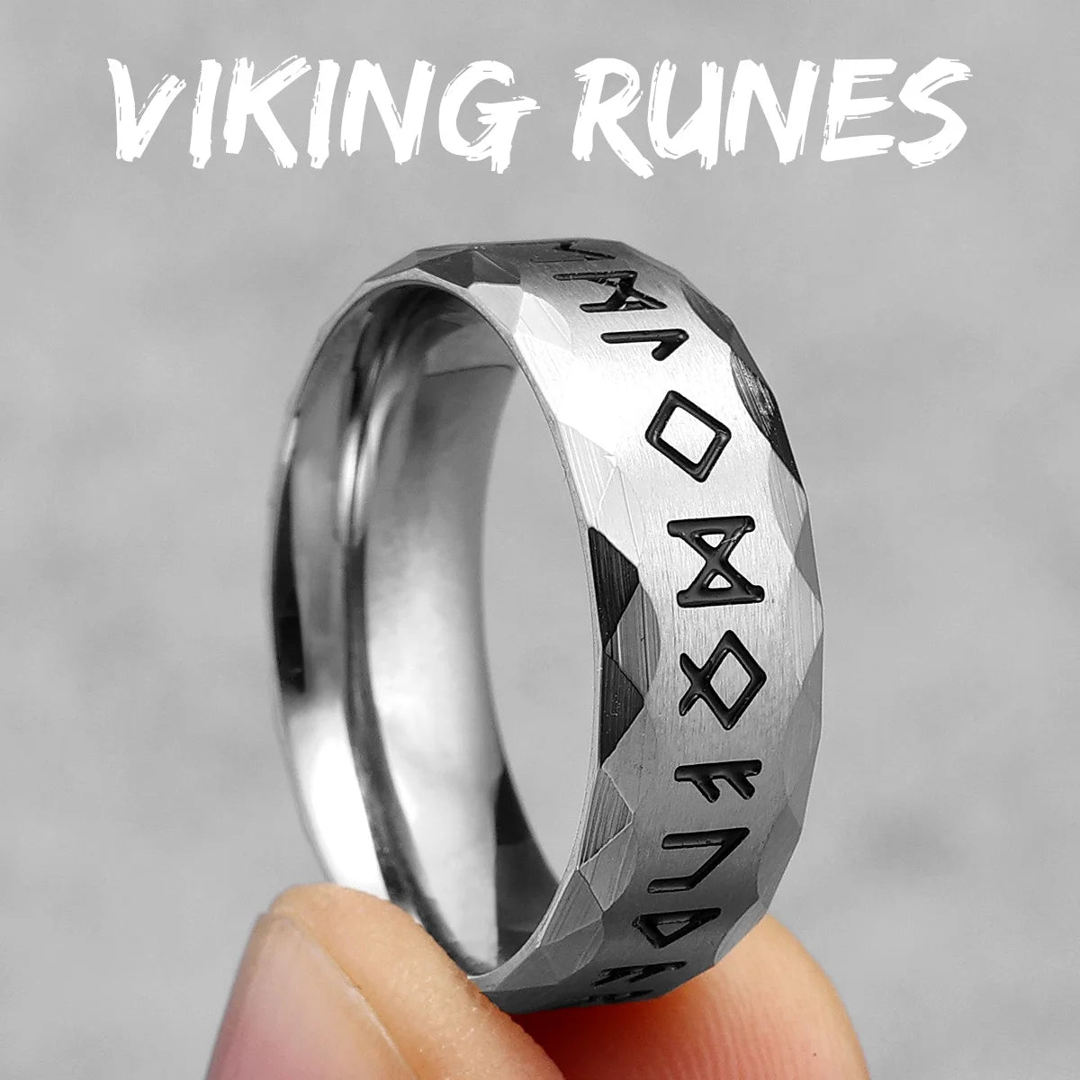 Silver ring with Viking runes held by a hand against a grey background